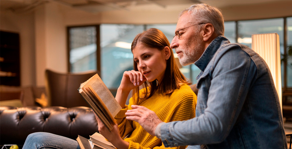 Convivencia Intergeneracional entre un hombre mayor y una mujer joven compartiendo un momento de lectura.