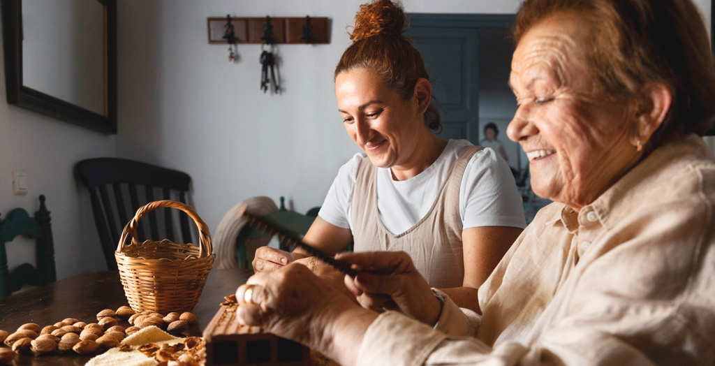 Dos personas, una mayor y una joven compartiendo un momento en una cocina de aspecto rural. 