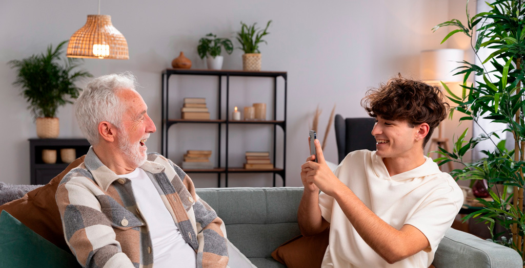 Convivencia entre una persona mayor y una persona joven, momento en el que el joven le hace una foto con el móvil a la persona mayor. 
